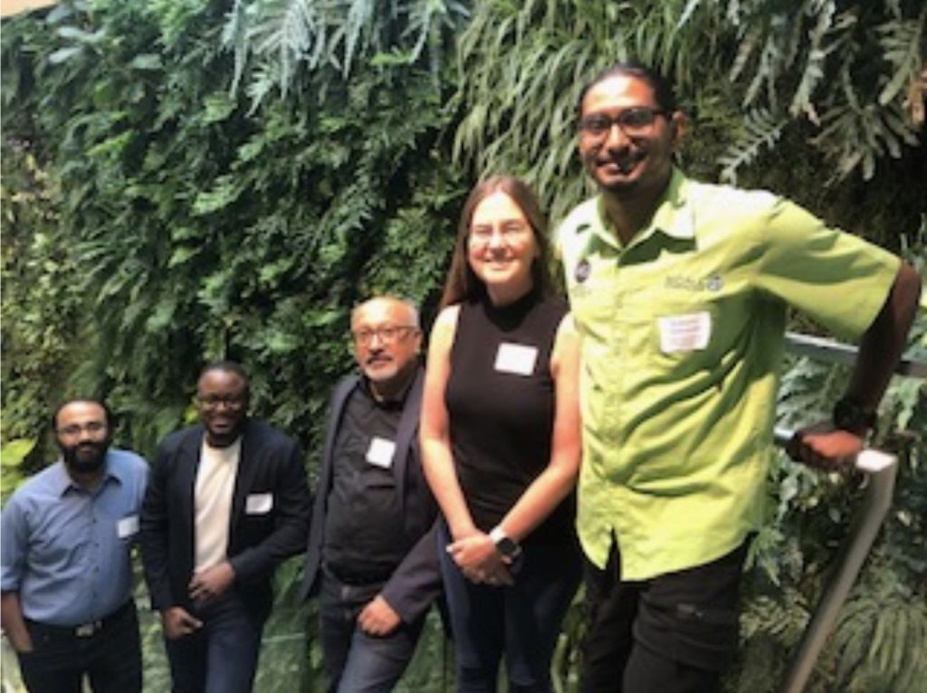 RCEI Affiliates, Shishir Chundawat, Kevon Rhiney, and Debashish Bhattacharya stand with Loretta Roberson (The Bell Center Marine Biological Laboratory) and Romario Anderson (University of the West Indies-Mona) against a wall of plants and greenery at Rutgers Harvest Cafe.